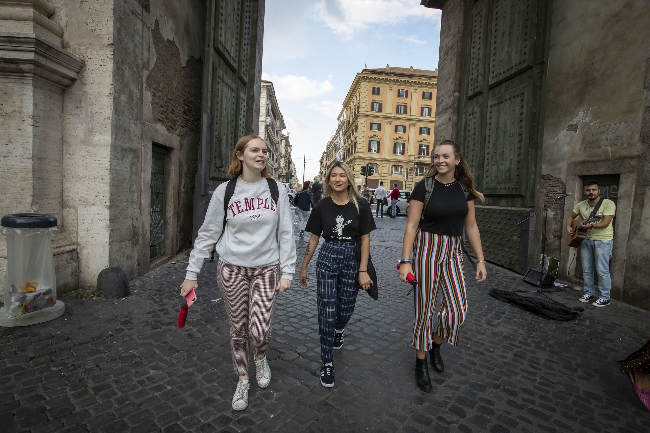 Three students wearing Temple gear walk the streets of Rome