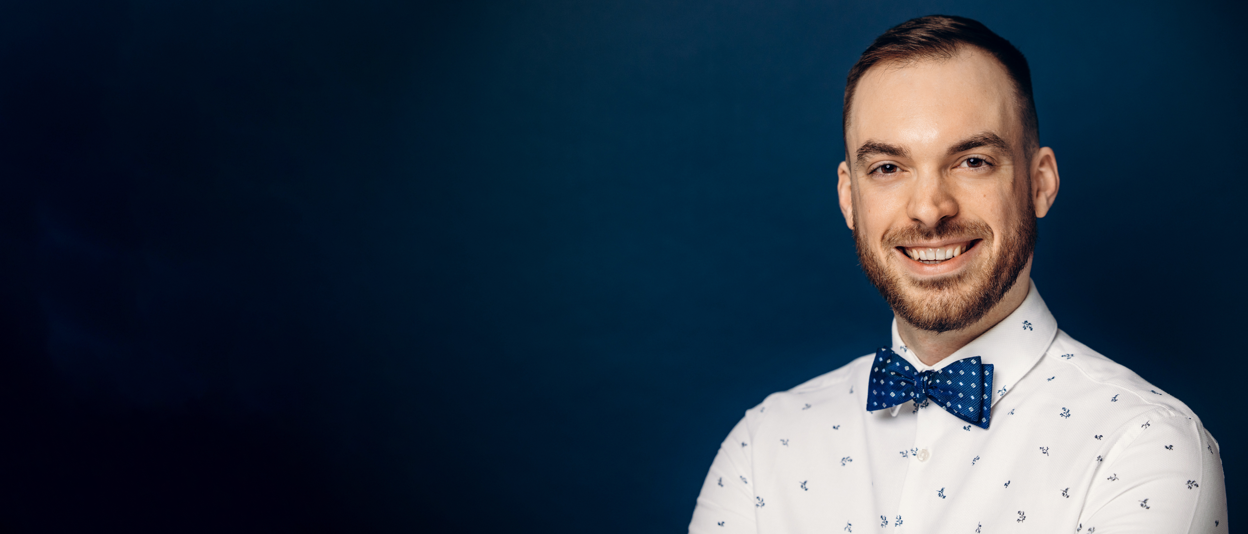 Eric Schroeckenthaler sits smiling against blue background in professional headshot