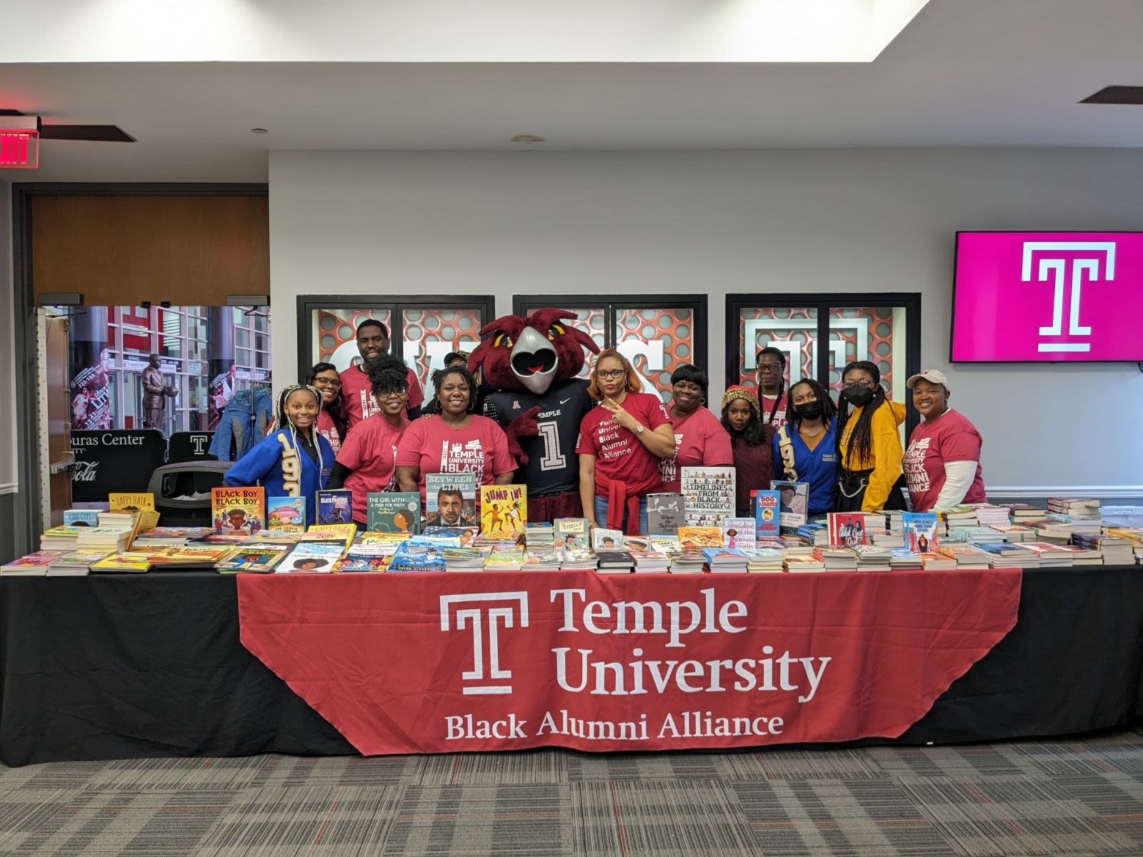 The members of TUBAA stand in front of table holding books for the book drive